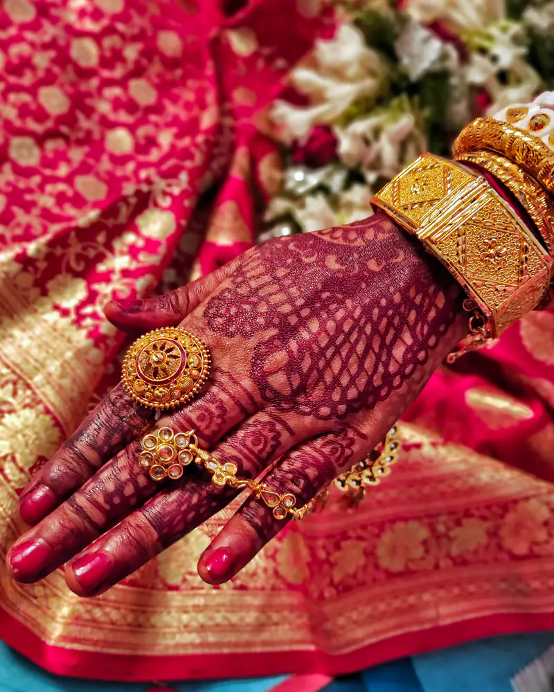Bride’s hand with intricate mehndi, a gold ring and a gold bangle