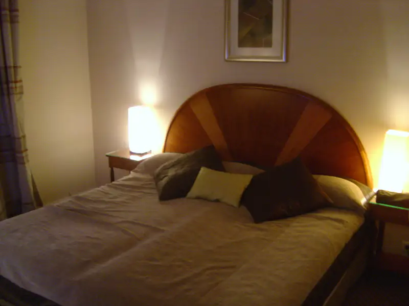 Warmly lit hotel bedroom with a curved wooden headboard