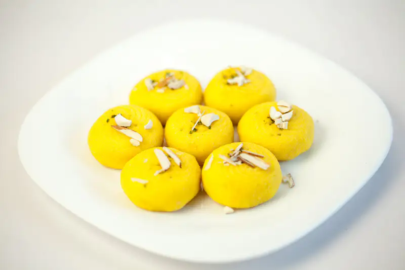 Saffron kesar pedas topped with almonds on a white plate