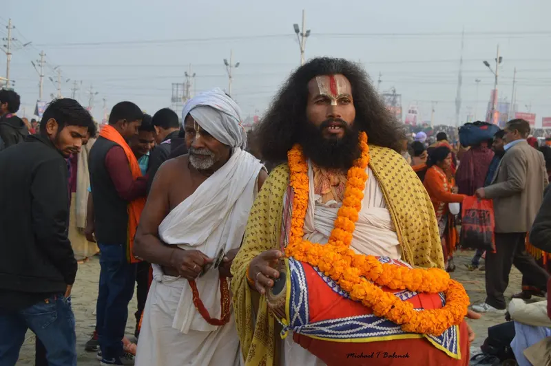 A sadhu in a marigold garland playing a drum at the Kumbh Mela